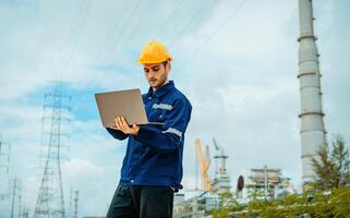 Worker in safety gear using laptop at industrial site with power lines in the background during the day photo