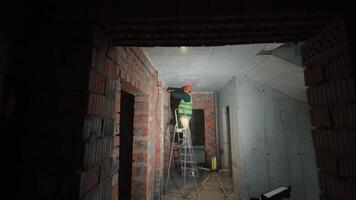 Worker on ladder installing cables inside unfinished building, Worker installing electrical wiring on ceiling of brick structure video