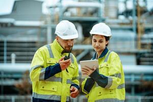 Workers collaborating at industrial site with communication device and tablet during project review photo