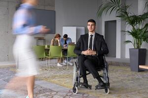A businessman in a wheelchair navigating through a busy office, surrounded by his colleagues who are actively engaged in their work and collaboration photo
