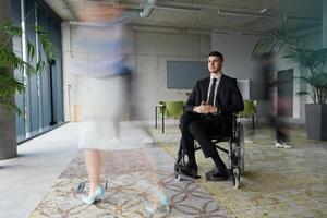 A businessman in a wheelchair navigating through a busy office, surrounded by his colleagues who are actively engaged in their work and collaboration photo