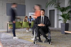 A businessman in a wheelchair navigating through a busy office, surrounded by his colleagues who are actively engaged in their work and collaboration photo