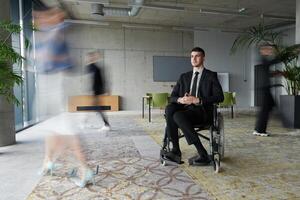 A businessman in a wheelchair navigating through a busy office, surrounded by his colleagues who are actively engaged in their work and collaboration photo
