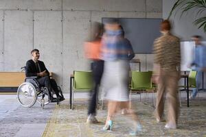 A diverse business team, working urgently around a conference table, collaborates on a meeting while their director, seated in a wheelchair, waits for their input photo