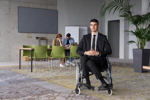 A businessman in a wheelchair navigating through a busy office, surrounded by his colleagues who are actively engaged in their work and collaboration photo