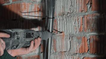 Worker drilling into a brick wall to install electrical conduit in a construction site, Hand of a worker operating a power drill to secure electrical wires along a red brick wall. video