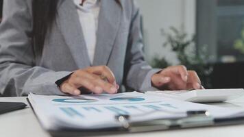 A woman in a business suit is using a calculator and pen to write on a paper video