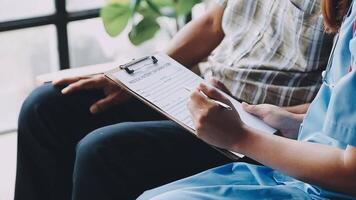 A nurse is writing on a clipboard while sitting next to a patient video