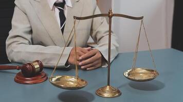 A man in a suit sits at a desk with a gavel and scales video