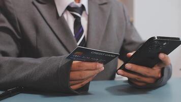 A man in a suit holding a credit card and a smartphone video