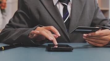 A man in a suit holding a credit card and a phone video