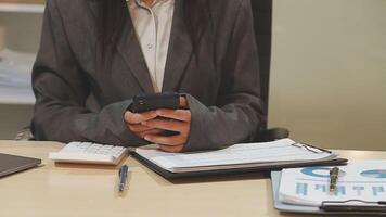 A woman in a business suit sitting at a desk with a cell phone video