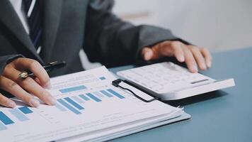 A person in a suit is using a calculator and a paper with graphs video