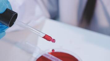 A person in a lab coat holding a tube with red liquid video