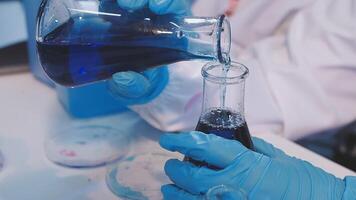A person in blue gloves pouring liquid into a beaker video