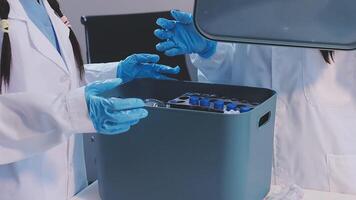 Two people in lab coats and gloves are holding a container video