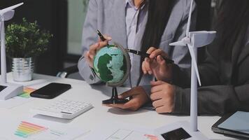 Business people working on a project with a globe and wind turbines video