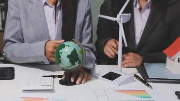 Two business people sitting at a table with a globe and wind turbine video