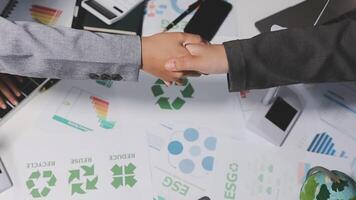Two business people shaking hands over a table with recycling symbols video