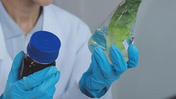 A woman in a lab coat holding a glass bottle with a green leaf video