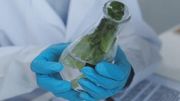 A person in a lab coat holding a plant in a glass video
