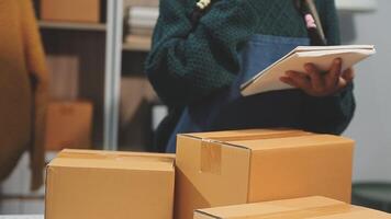 A woman in an apron is holding a notebook and looking at a stack of boxes video