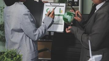 Two businesswomen in suits holding a clipboard and looking at a chart video