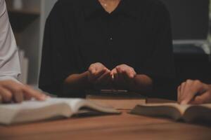 A group of people sitting at a table with their hands on the bible photo