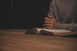 Man praying with bible and cross on wooden table photo