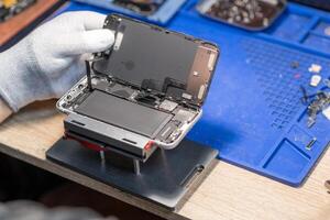 A technician performs a battery replacement on a mobile device, showcasing tools and parts in a well-organized repair workspace photo