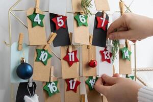 Number on craft paper notes with tasks before Christmas holidays. Female making kraft paper for handmade advent calendar Made with your own hands step by step DIY crafts do it yourself photo