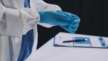 A person in a white coat and blue gloves is holding a clipboard video
