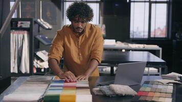 Male fashion designer interior decorator choosing samples color fabric at workshop Arabian Indian man guy tailor stylist dressmaker choose compare woolen material cloth collection clothes accessories video