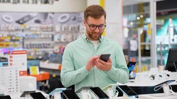 Happy young man choosing a new smartphone in a tech store video