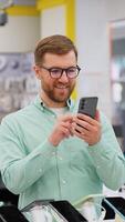 Happy young man choosing a new smartphone in a tech store. Vertical video