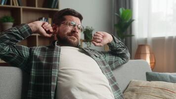 Smiling lazy relaxing resting Caucasian man guy male homeowner relax at couch sofa own rent home loan mortgage yawning stretching hands sleepy napping yawn sleep calm weekend indoors smile insomnia video