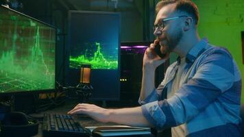 Positive Caucasian man worker male guy employer smile typing keyboard computer talking mobile phone. Happy crypto trader discussing multitask show thumb up excellent statistic home night working neon video