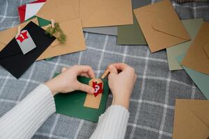 Number on craft envelopes notes with tasks before Christmas holidays. Female making kraft paper for handmade advent calendar Made with your own hands step by step DIY crafts do it yourself photo
