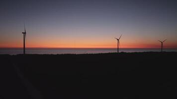 Silhouettes of wind turbines stand tall against a vibrant sunset sky, generating renewable energy video