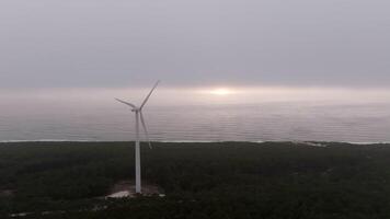Wind turbine slowly rotates near the ocean, creating a serene scene at sunset with vibrant colors in the sky video