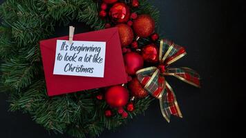 Greeting card with IT'S BEGINNING TO LOOK A LOT LIKE CHRISTMAS text on handmade Christmas wreath. Festive mood new year celebration. Postcard decoration decor top view, flat lay photo
