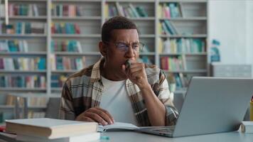 Tired sleepy bored African American man yawning male student laptop write notepad lesson online learning studying university library high school computer e-learning guy college education technology video