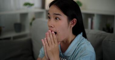 Handheld shot, An attractive young woman is intently watching something on TV and shows signs of extreme excitement and joy while sitting on sofa in the living room at home. video