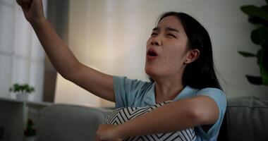 Handheld low angle view shot, An attractive young woman is intently watching something on TV and shows signs of extreme excitement and joy while sitting on sofa in the living room at home. video