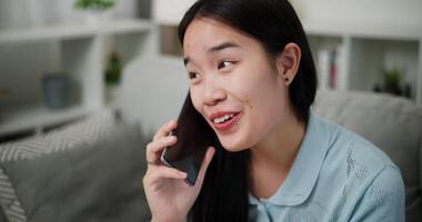 Handheld selective focus shot, Cheerful young woman is having fun talking on smartphone with her friend, smiling and laughing happily while sitting on the sofa in the living room at home. video