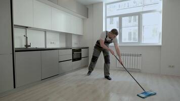 A builder in uniform washes the floor in a new apartment. The concept of construction and repair. video