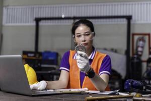Asian woman technician engineer working designing mechanical parts engineering with laptop and example small gear in hand at industrial workshop. photo