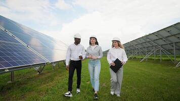 Three multiracial engineers walking in solar station checking solar panels setup video