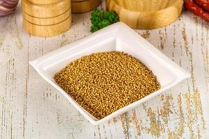 A bowl of mustard seeds and spices on a wooden table photo
