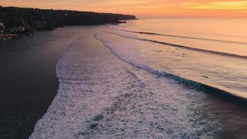 Ocean with perfect surfing waves on Impossibles beach with evening warm sunlight, drone view video